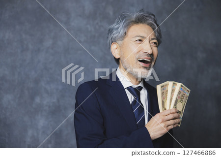 Smiling senior businessman holding a stack of bills 127466886