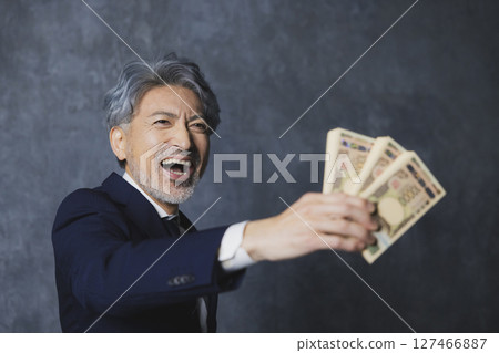 Smiling senior businessman holding a stack of bills Smiling senior businessman holding a stack of bills 127466887