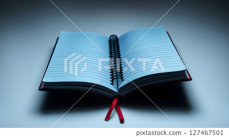 An open notebook with blue lined pages, a red ribbon, and a black spiral binding on a desk 127467501