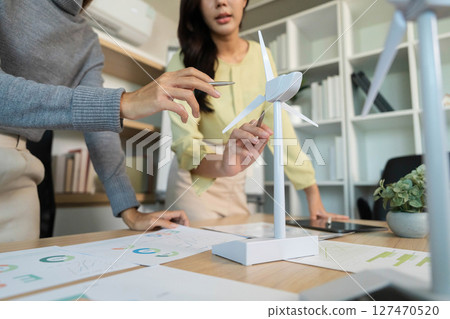 ESG Development. Team collaborating on sustainable energy solutions with wind turbine model. ESG Development. Team collaborating on sustainable energy solutions with wind turbine model. 127470520