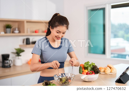 ESG and Healthy Eating. Woman mixing fresh salad in a bright kitchen. 127470632