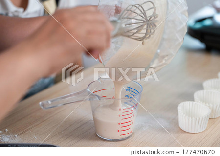 Family Cooking Fun. A child pouring batter into a measuring cup with mom's guidance. Family Cooking Fun. A child pouring batter into a measuring cup with mom's guidance. 127470670
