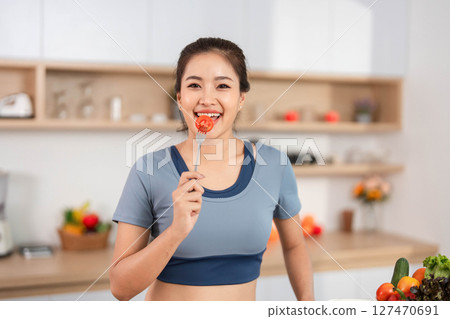 ESG and Nutrition. Woman enjoying fresh tomato in a modern kitchen. 127470691