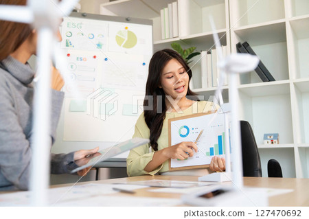 ESG Strategy Meeting. Businesswoman presenting sustainability metrics and charts in a modern office. 127470692