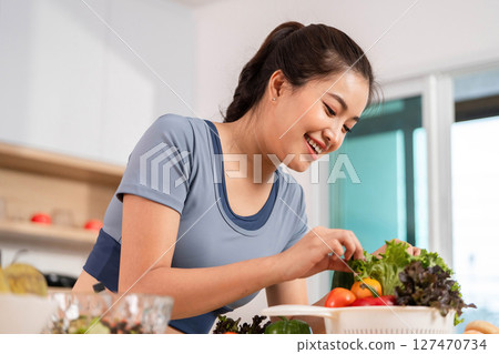 ESG and Healthy Meal Prep. Woman smiling while handling fresh vegetables in her kitchen. 127470734