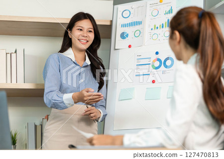 Engaging Business Presentation. Female professional explaining data insights to colleague in office. Engaging Business Presentation. Female professional explaining data insights to colleague in office. 127470813