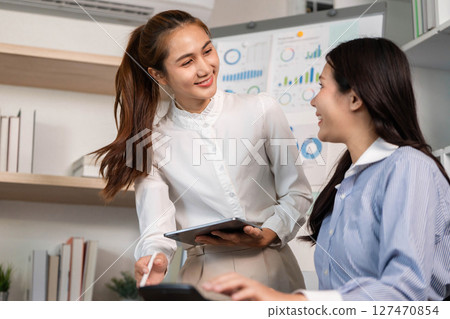Team Collaboration. Businesswomen sharing insights while reviewing analytics in a bright office. 127470854