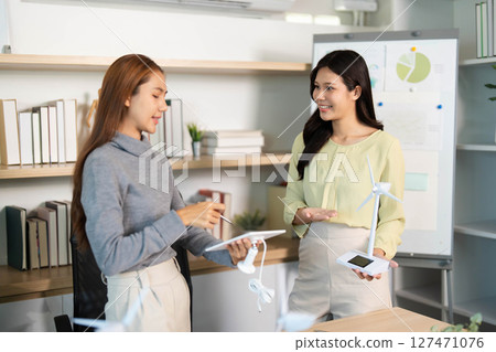 ESG Focus. Two women presenting renewable energy solutions in a collaborative office environment. ESG Focus. Two women presenting renewable energy solutions in a collaborative office environment. 127471076