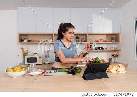 ESG and Cooking. Woman preparing a healthy meal while using a tablet in a modern kitchen. 127471078