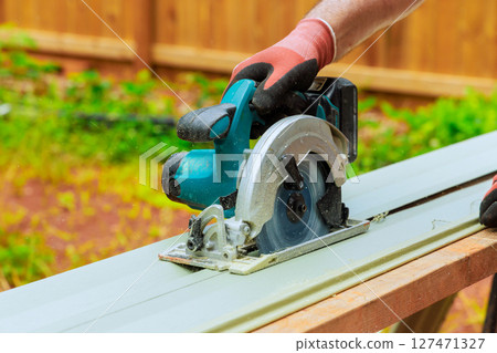 Worker uses circular saw to cut PVC siding plank in backyard during works day construction skills 127471327