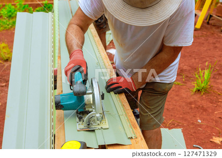 Carpenter using power saw to cut sheets for outdoor construction project in sunny garden setting 127471329