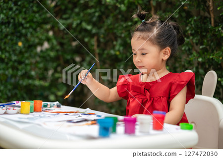 happy toddler girl painting watercolor in paper at backyard. happy toddler girl painting watercolor in paper at backyard. 127472030