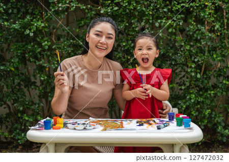 happy mother and toddler girl painting watercolor in paper at backyard. happy mother and toddler girl painting watercolor in paper at backyard. 127472032