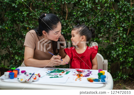 happy mother and toddler girl painting watercolor in paper at backyard. happy mother and toddler girl painting watercolor in paper at backyard. 127472033