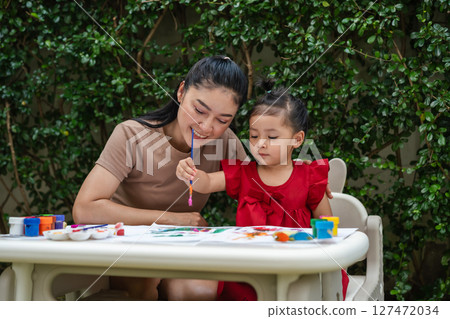 happy mother and toddler girl painting watercolor in paper at backyard. 127472034