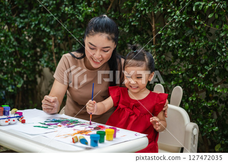 happy mother and toddler girl painting watercolor in paper at backyard. 127472035