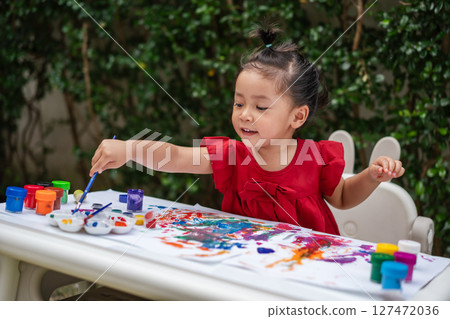 happy toddler girl painting watercolor in paper at backyard. happy toddler girl painting watercolor in paper at backyard. 127472036