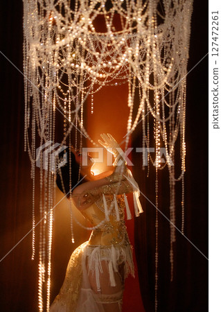 Young woman in vintage corset costume posing under chandelier on dark background Young woman in vintage corset costume posing under chandelier on dark background 127472261