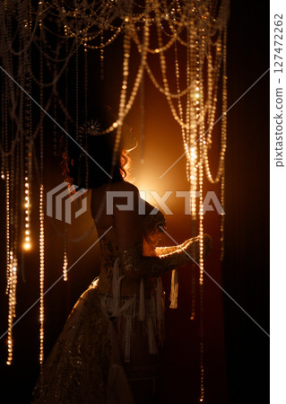 Young woman in vintage corset costume posing under chandelier on dark background Young woman in vintage corset costume posing under chandelier on dark background 127472262