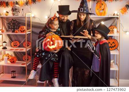 Family With Children Celebrating Halloween Party At Home Reading A Book Together In Costumes Family With Children Celebrating Halloween Party At Home Reading A Book Together In Costumes 127473902