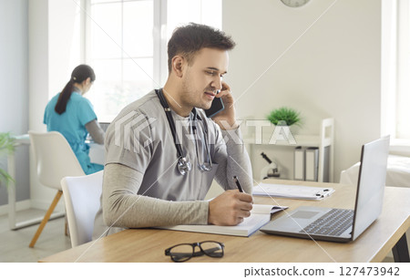 Positive Male Doctor Or Nurse Answering Phone Call While Working Online Positive Male Doctor Or Nurse Answering Phone Call While Working Online 127473942