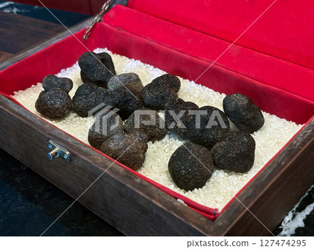 A collection of dark truffle rests in a luxurious wooden box lined with rice, showcasing their unique shape and rich texture at a gourmet market A collection of dark truffle rests in a luxurious wooden box lined with rice, showcasing their unique shape and rich texture at a gourmet market 127474295