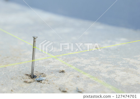 A close-up of a nail driven into rough concrete with intersecting yellow lines, representing detailed construction work for house tiling projects. A close-up of a nail driven into rough concrete with intersecting yellow lines, representing detailed construction work for house tiling projects. 127474701