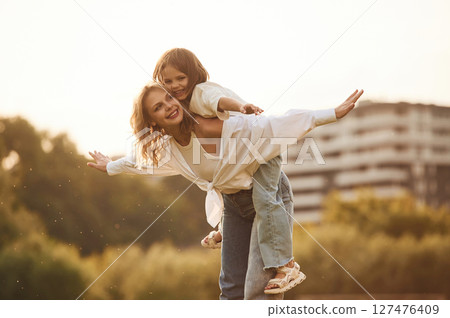 Sitting on the mother shoulders. Woman with her little daughter are on the summer field together 127476409