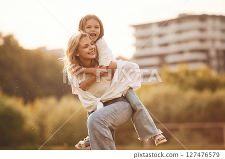 Sitting on the mother shoulders. Woman with her little daughter are on the summer field together 127476579