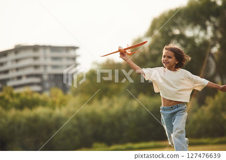 Running forward. Happy little girl is playing with toy plane outdoors 127476639