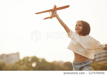 Running forward. Happy little girl is playing with toy plane outdoors 127476640