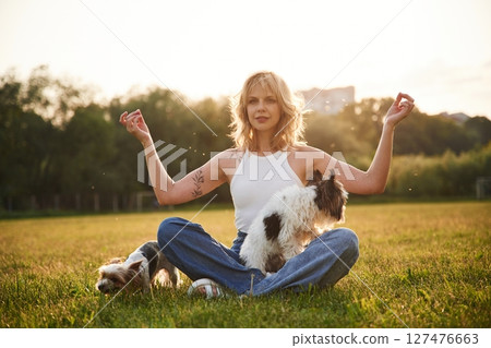 Sitting in yoga lotus pose. Young woman is with two little dogs on the summer field Sitting in yoga lotus pose. Young woman is with two little dogs on the summer field 127476663