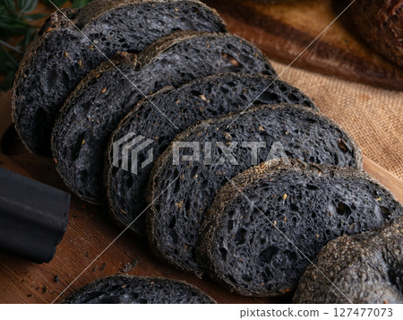 Fresh baked black charcoal sourdough ciabatta bread sliced on wooden board. 127477073