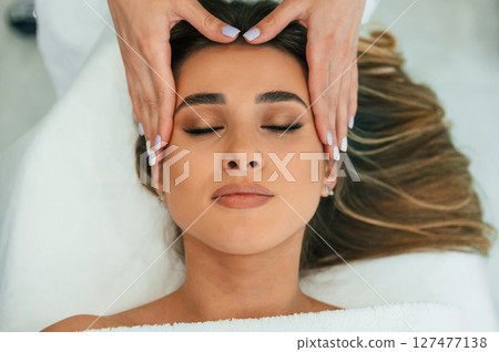 With eyes closed, doing massage. Woman face getting facial care by beautician hands at spa salon With eyes closed, doing massage. Woman face getting facial care by beautician hands at spa salon 127477138