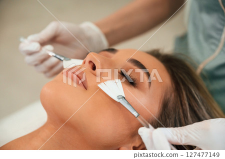 Cleaning skin by brushes. Woman face getting facial care by beautician hands at spa salon 127477149