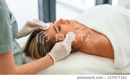 Cleaning skin by using cotton pad or sponge. Woman face getting facial care by beautician hands at spa salon Cleaning skin by using cotton pad or sponge. Woman face getting facial care by beautician hands at spa salon 127477161