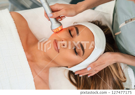 Apparatus for galvanization is used. Woman face getting facial care by beautician hands at spa salon 127477175