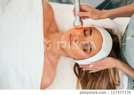 Apparatus for galvanization is used. Woman face getting facial care by beautician hands at spa salon 127477176