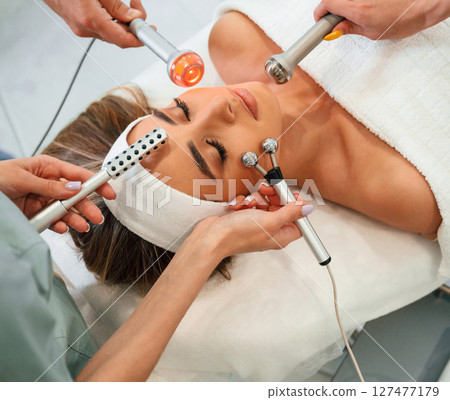 Many of different cosmetitian tools. Woman face getting facial care by beautician hands at spa salon 127477179