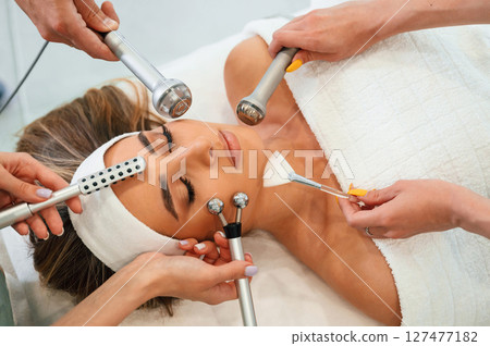 Hands are holding bunch of cosmetitian tools. Woman face getting facial care by beautician hands at spa salon Hands are holding bunch of cosmetitian tools. Woman face getting facial care by beautician hands at spa salon 127477182