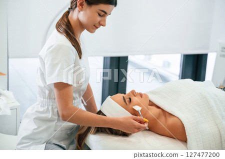 Side view. Woman face getting facial care by beautician hands at spa salon 127477200