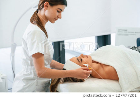 Side view. Woman face getting facial care by beautician hands at spa salon 127477201