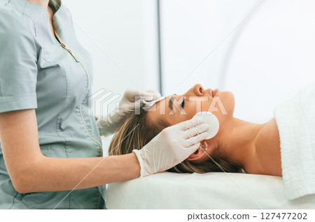 Side view. Woman face getting facial care by beautician hands at spa salon 127477202