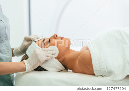 Side view. Woman face getting facial care by beautician hands at spa salon 127477204
