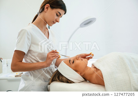 Woman face getting facial care by beautician hands at spa salon 127477205