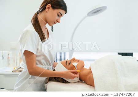 Lying down. Using brushes. Woman face getting facial care by beautician hands at spa salon Lying down. Using brushes. Woman face getting facial care by beautician hands at spa salon 127477207