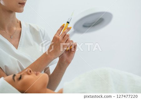 Holding a syringe. Woman face getting facial care by beautician at spa salon 127477220