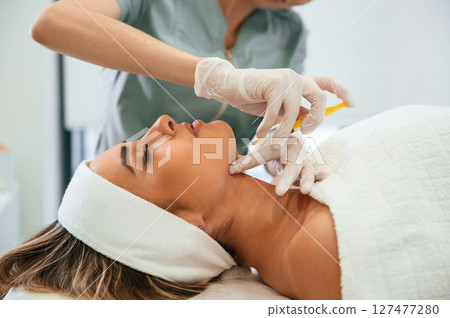 Yellow colored syringe, making injection. Woman face getting facial care by beautician hands at spa salon Yellow colored syringe, making injection. Woman face getting facial care by beautician hands at spa salon 127477280