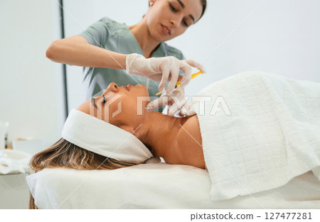 Yellow colored syringe, making injection. Woman face getting facial care by beautician hands at spa salon Yellow colored syringe, making injection. Woman face getting facial care by beautician hands at spa salon 127477281