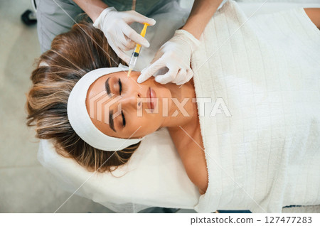Injection into the face skin. Woman face getting facial care by beautician hands at spa salon Injection into the face skin. Woman face getting facial care by beautician hands at spa salon 127477283